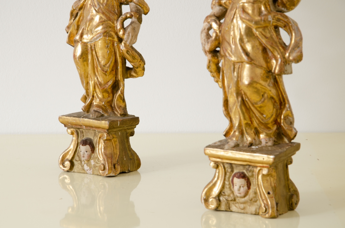 Coppia di angeli in legno laccato e dorato che reggono una cornucopia con corona in metallo dorato.   Italia centrale, epoca Barocco, seconda metà del XVII secolo.