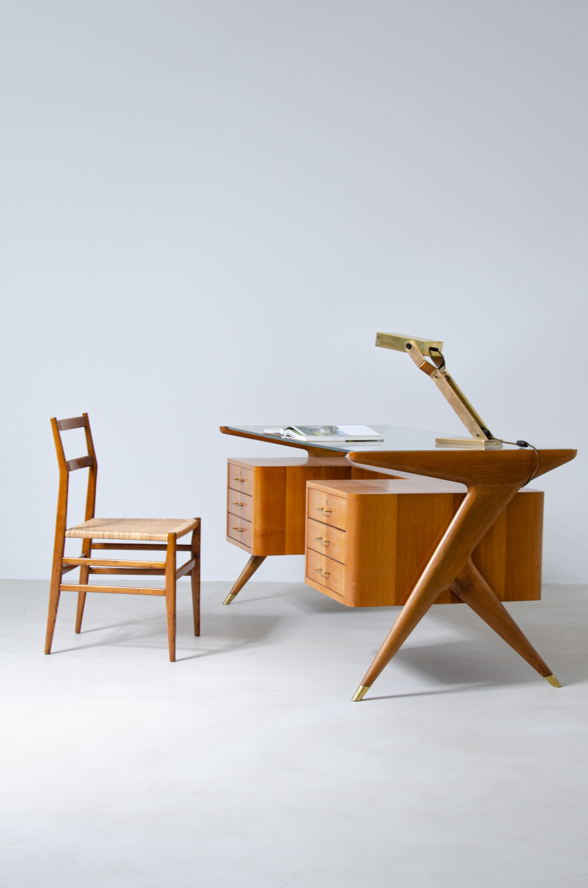 Writing table in blond wood with thick glass top and sculptural side uprights with brass tips.  1950's Italian manufacture.