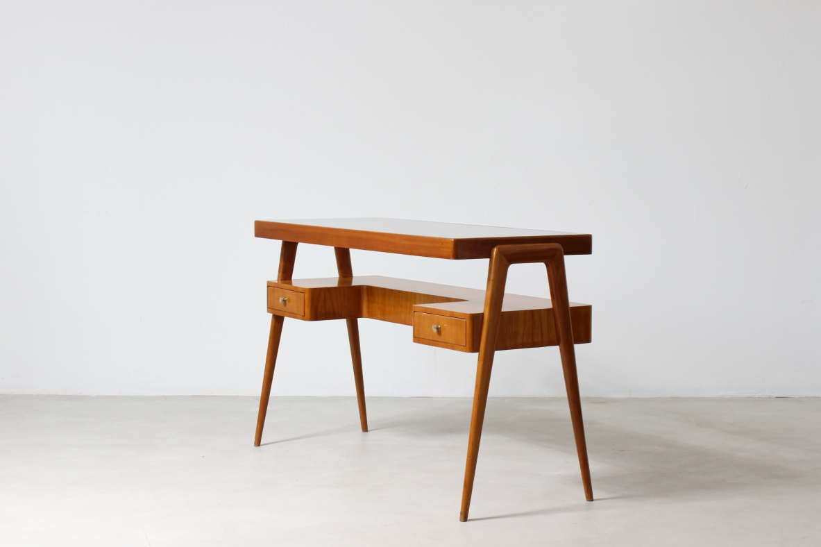 Small desk in blond wood with glass top and shaped shelf with two drawers on the front.