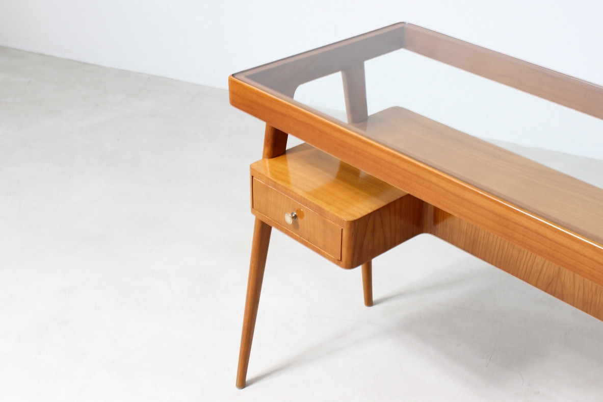 Small desk in blond wood with glass top and shaped shelf with two drawers on the front.