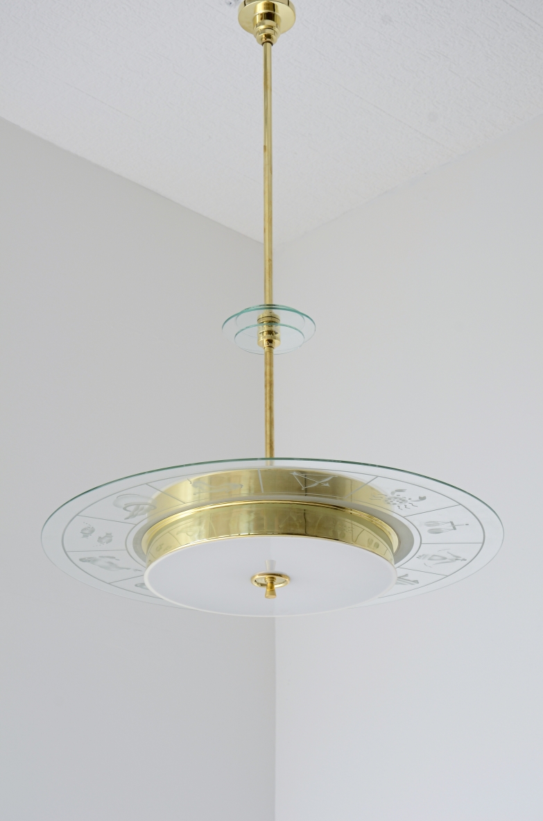 Grande lampadario in ottone con vetro molato e decorato con i disegni dello zodiaco e due vetri bianco lattimo. Stelo in ottone con tre dischi in vetro trasparente molato.  Manifattura Brusotti Milano, 1930-40ca.