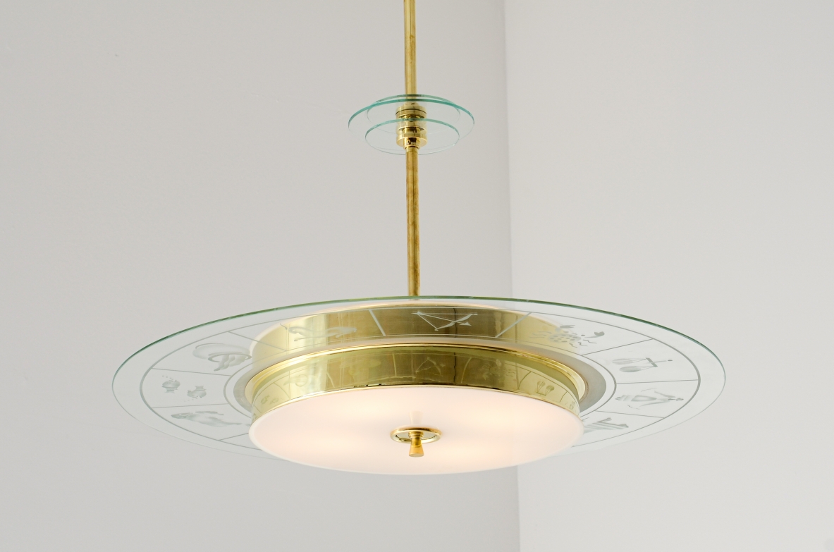 Grande lampadario in ottone con vetro molato e decorato con i disegni dello zodiaco e due vetri bianco lattimo. Stelo in ottone con tre dischi in vetro trasparente molato.  Manifattura Brusotti Milano, 1930-40ca.