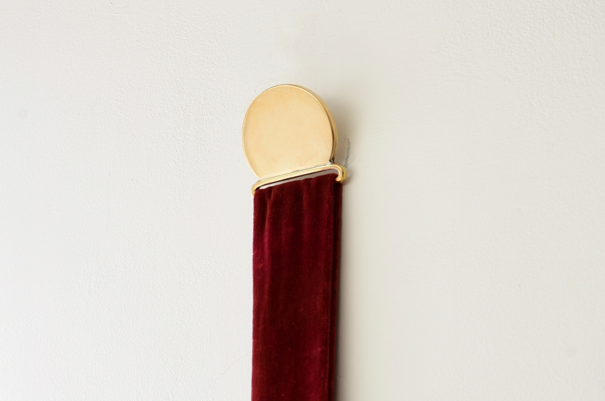 Specchiera in ottone sagomato appesa a un nastro in velluto originale e fissata a parete mediante un disco in ottone.  Manifattura italiana anni 50/60ca.