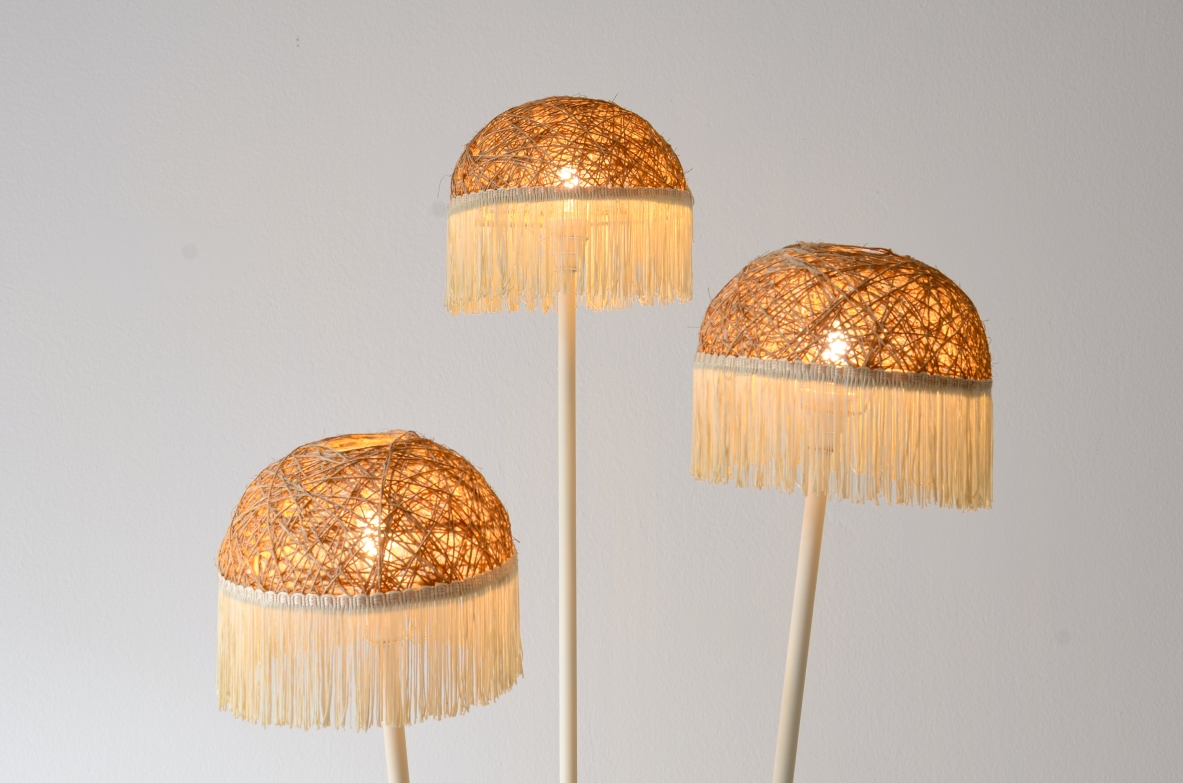 Lampada da terra a tre bracci in metallo laccato con cappelli in rattan e frange in tessuto.Manifattura italiana 1950ca.