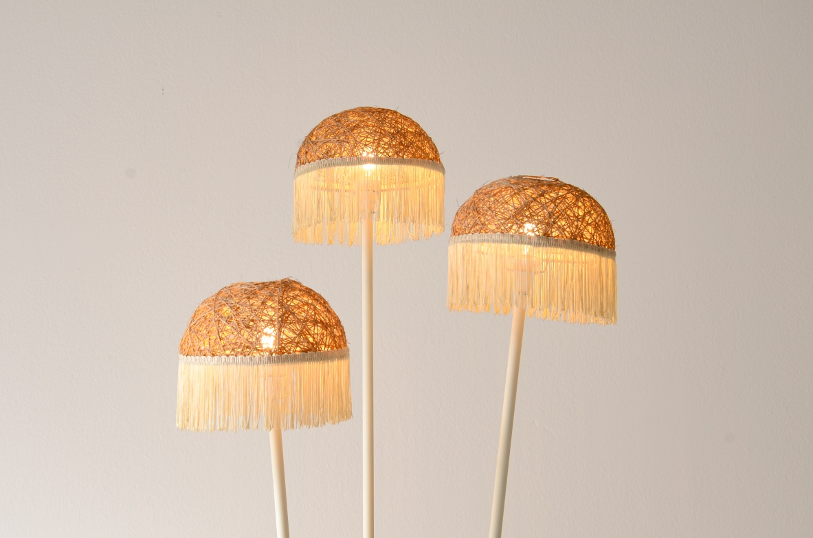 Lampada da terra a tre bracci in metallo laccato con cappelli in rattan e frange in tessuto.Manifattura italiana 1950ca.